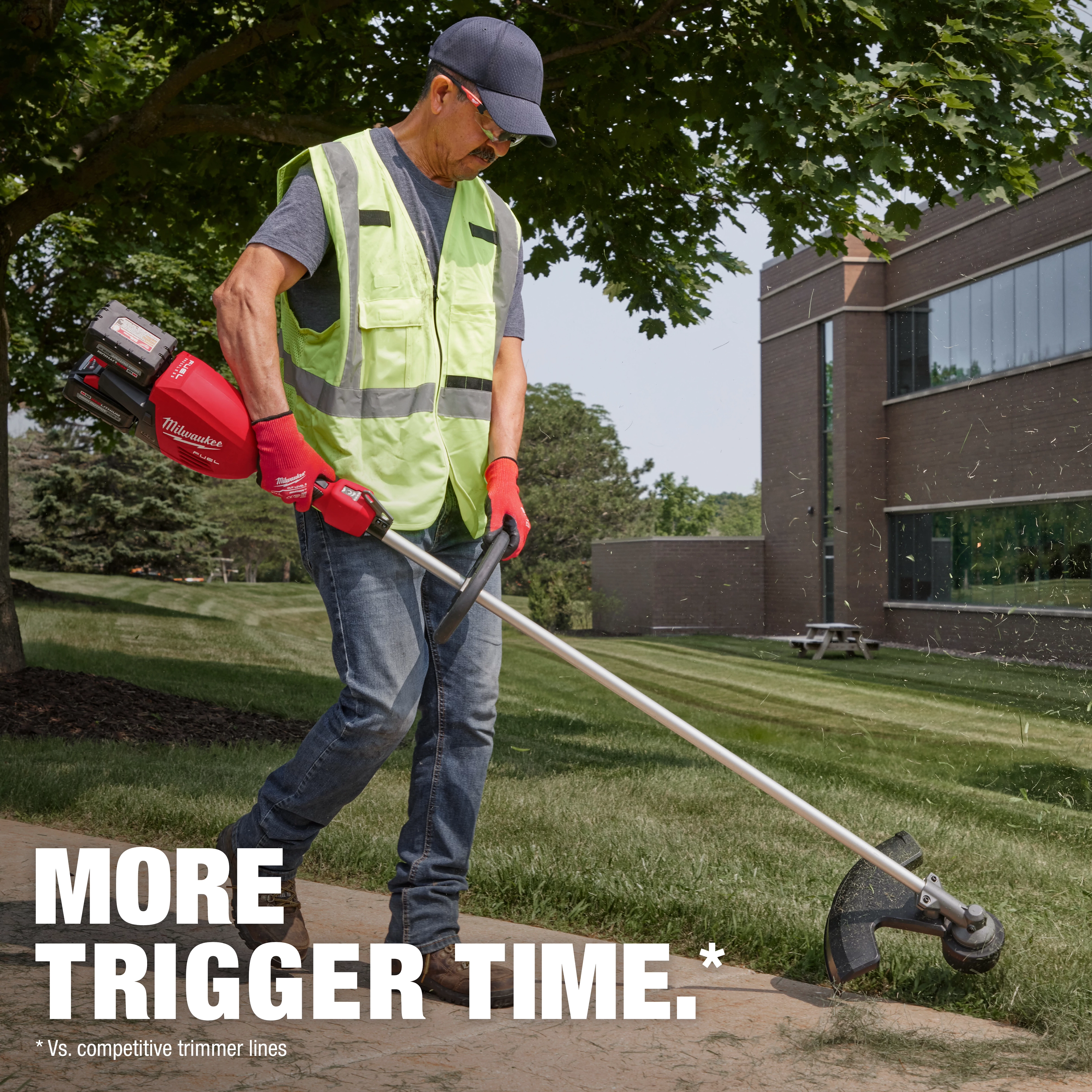 Person wearing a safety vest using a red Milwaukee string trimmer on a lawn near a building. Text: "MORE TRIGGER TIME."