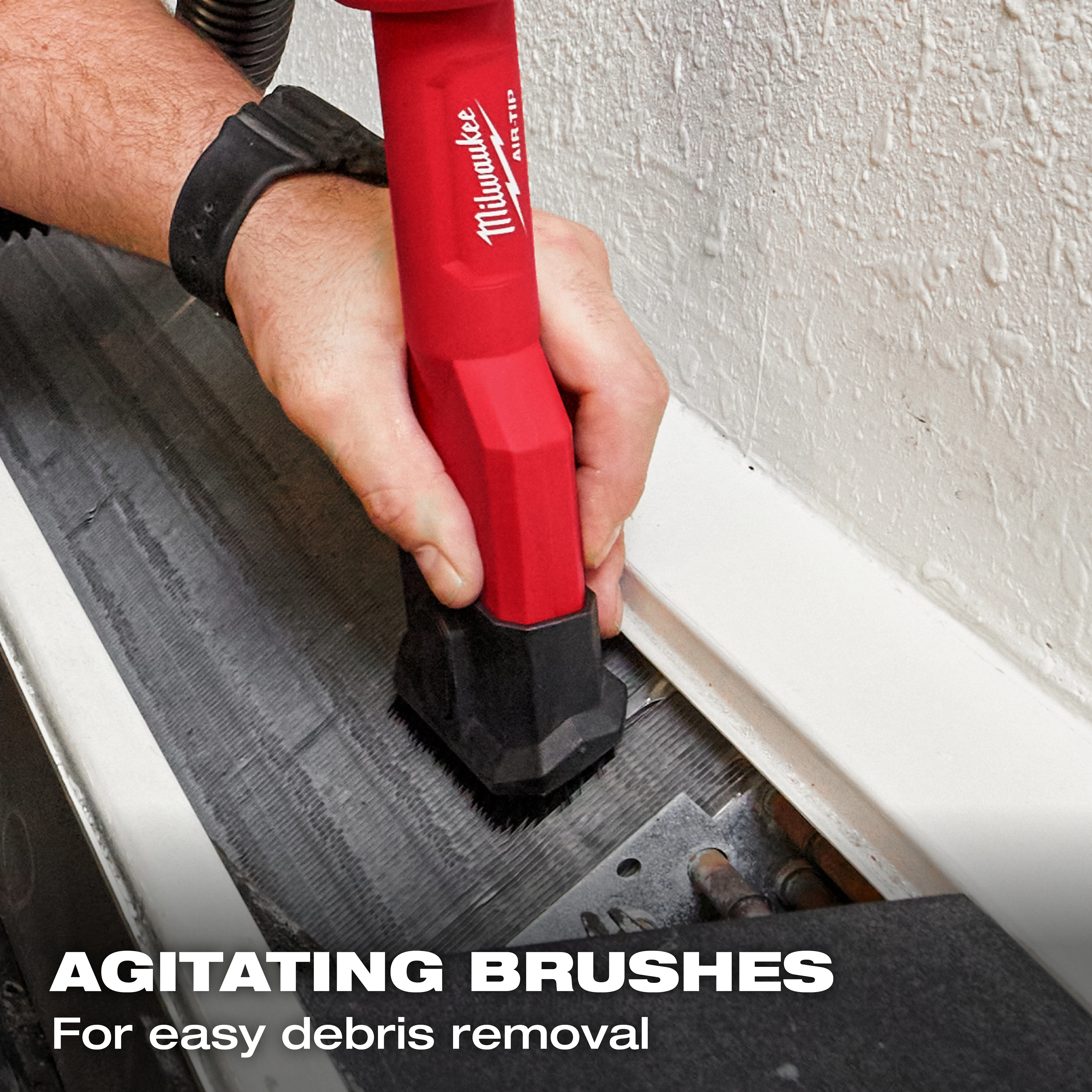 A person using the AIR-TIP™ 2-in-1 Utility Brush Tool to clean debris. The tool has a red handle, labeled with the Milwaukee brand. The text "AGITATING BRUSHES For easy debris removal" appears at the bottom.