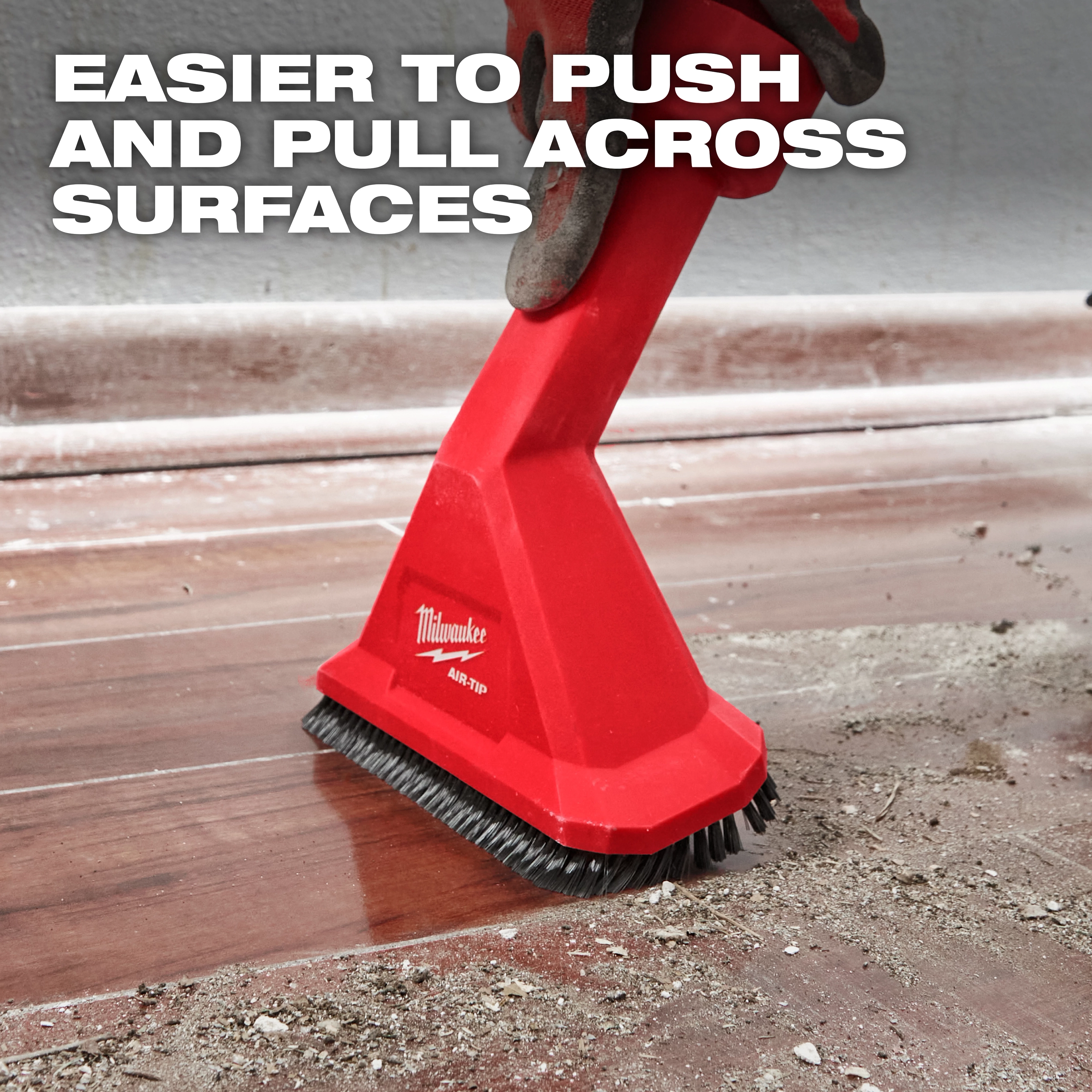 A red Milwaukee AIR-TIP™ Rocking Utility Nozzle with Brushes is shown being pushed across a dirty floor. Text at the top states: "Easier to Push and Pull Across Surfaces." The nozzle has bristles at the base for effective cleaning.