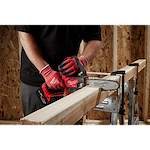 A person using a red Milwaukee chainsaw to cut a wooden beam supported by a sawbuck.