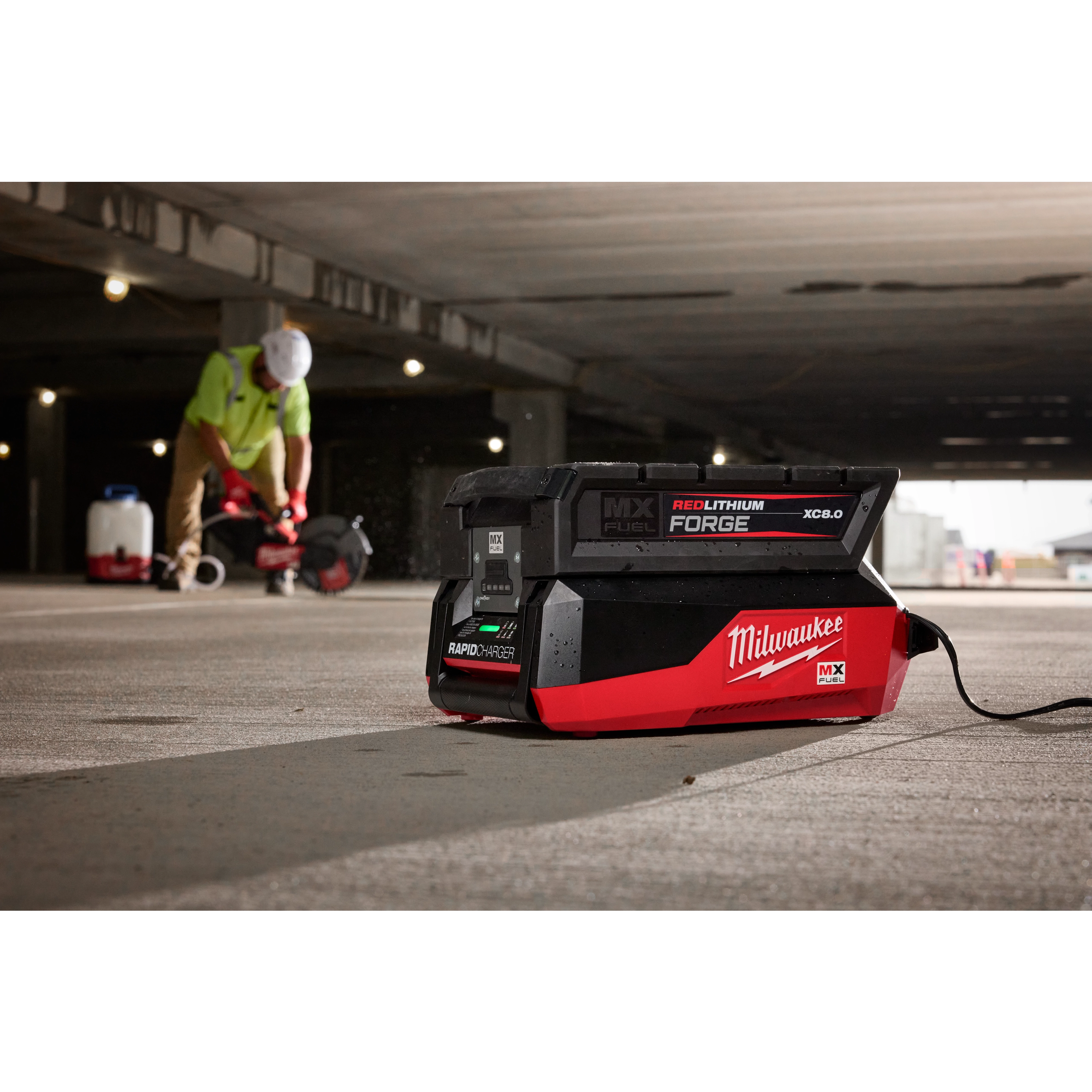 Milwaukee Rapid Charger on concrete floor, with a worker in safety gear using equipment in the background.