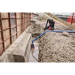 An MX FUEL™ Portable Pump Power Base and an MX FUEL™ 1HP 2" Submersible Pump Kit in use at a construction site. The submersible pump is placed in a water-filled trench, connected to the power base via a blue hose.