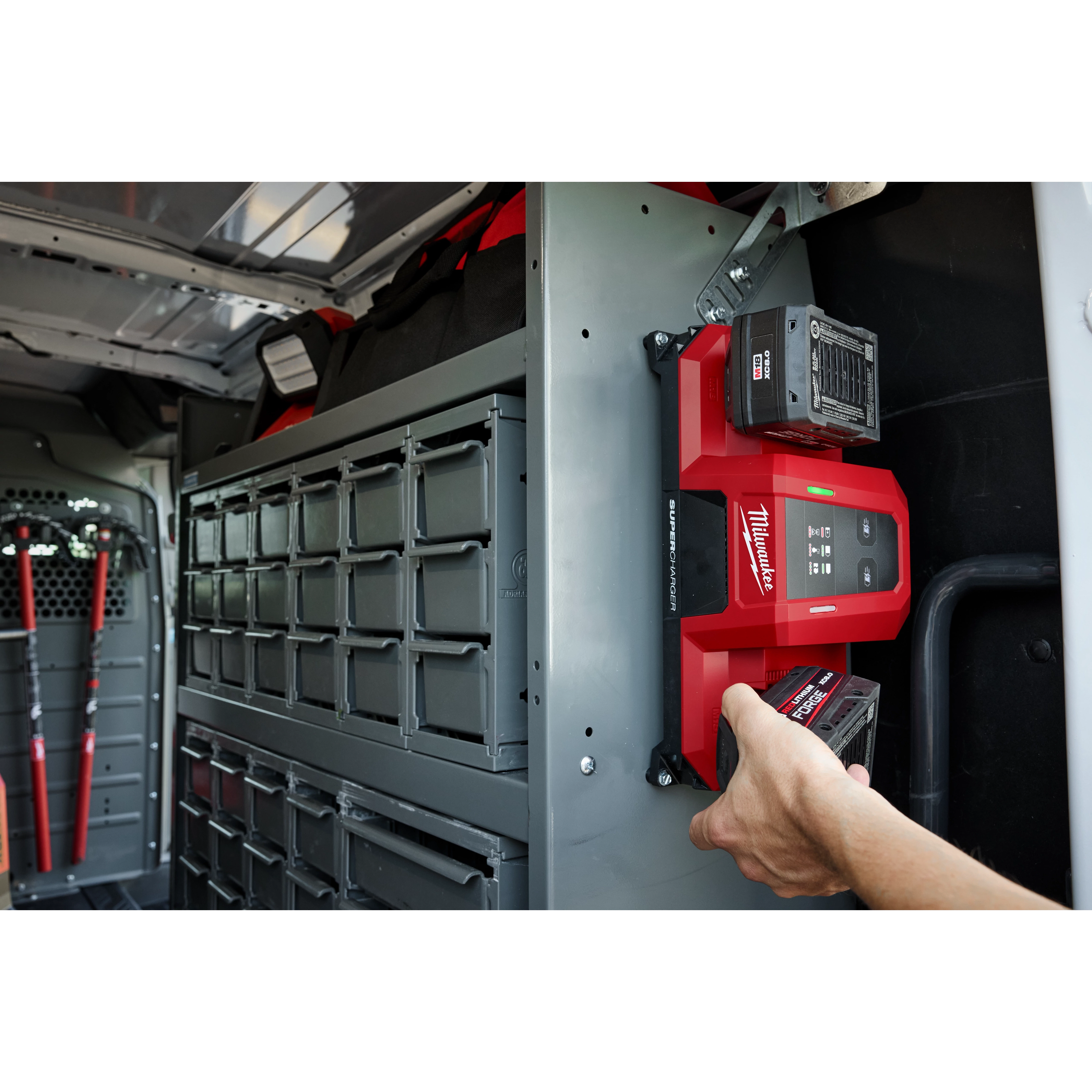 Person placing a battery into an M18 Dual Bay Simultaneous Super Charger mounted inside a vehicle with organized storage compartments.