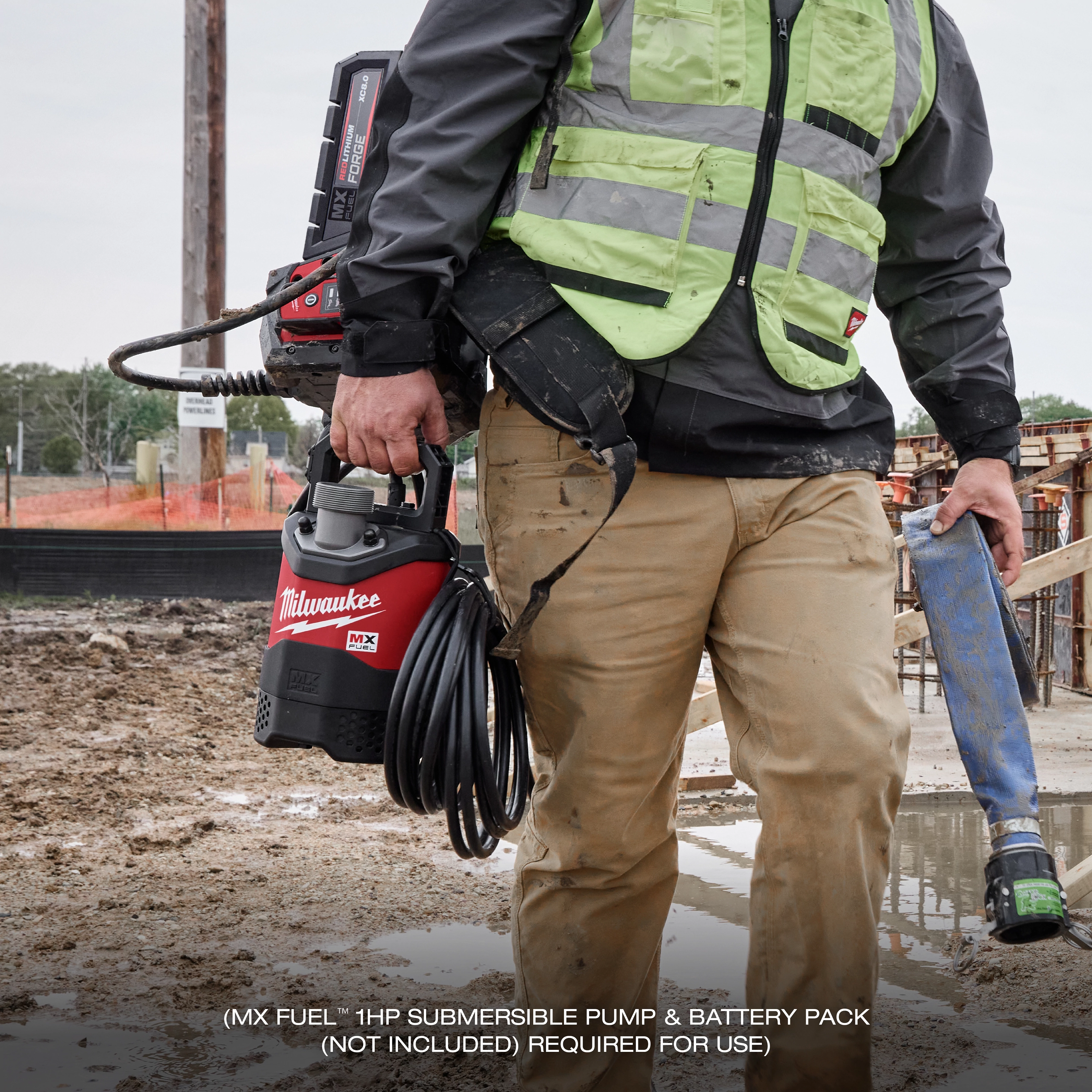 A construction worker holds the MX FUEL™ Portable Pump Power Base in a muddy construction site. The power base is red and black with the Milwaukee logo, and the worker wears a high-visibility vest and carries tools. The text at the bottom reads "(MX FUEL™ 1HP SUBMERSIBLE PUMP & BATTERY PACK (NOT INCLUDED) REQUIRED FOR USE)."