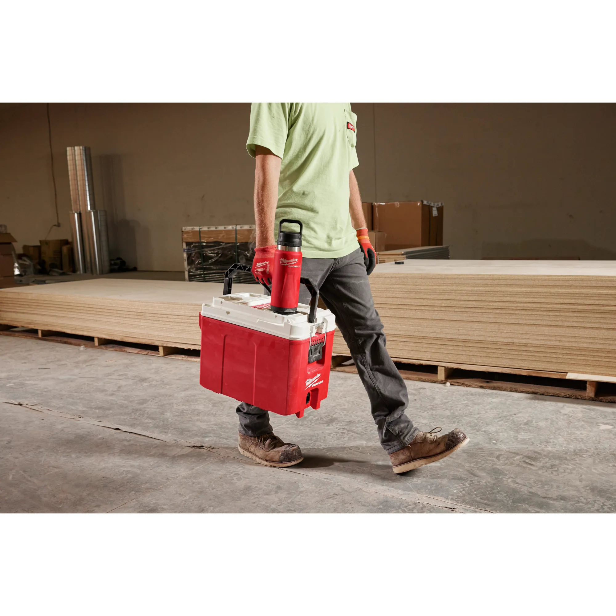 Image of a worker carrying a Milwaukee Cooler with a PACKOUT Insulated Bottle with Chug Lid in red