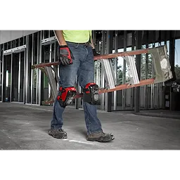 Person wearing knee pads and gloves, carrying a ladder inside a partially constructed building.