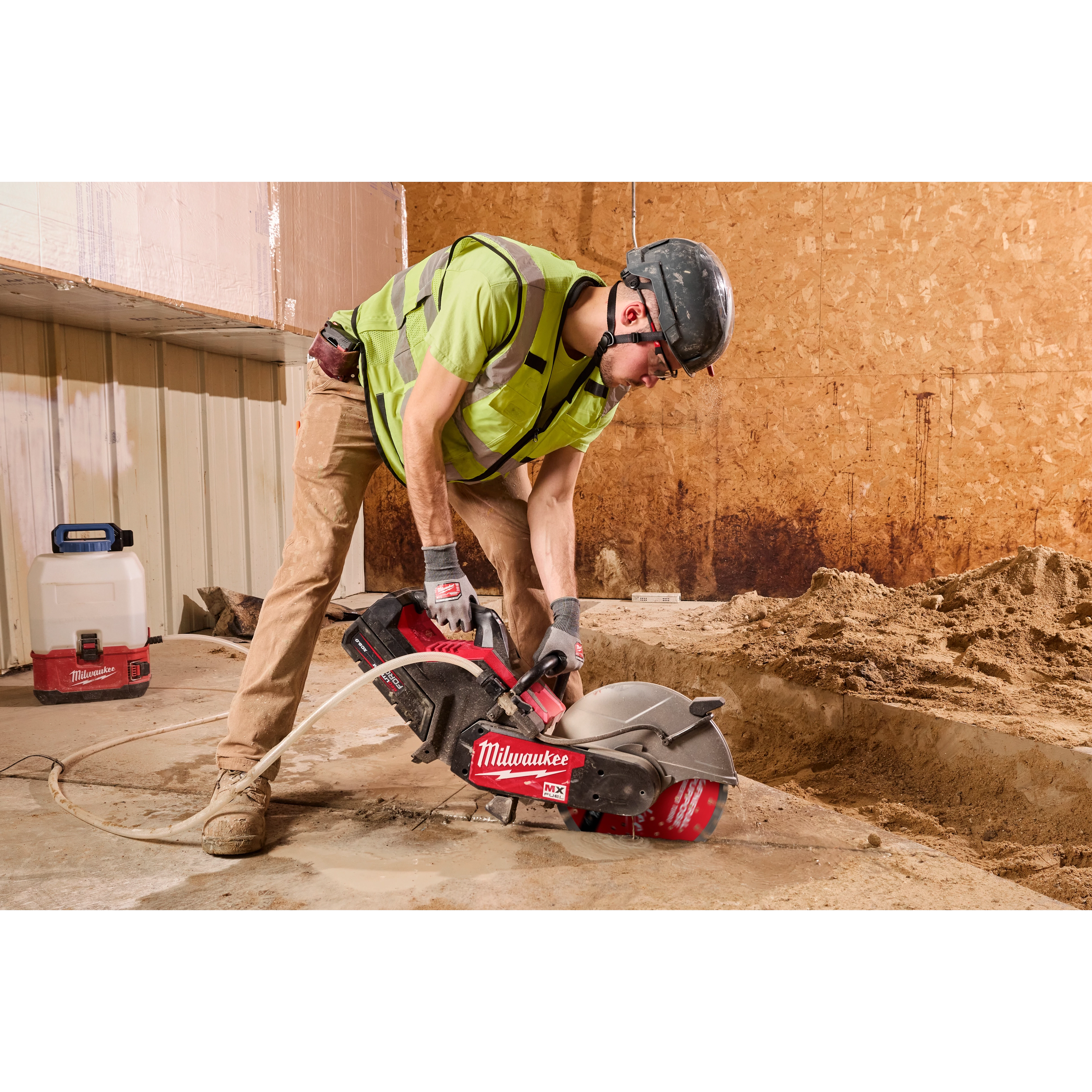 A construction worker wearing a helmet and hi-vis vest uses a power saw equipped with a 14" DIAMOND ULTRA™ Segmented Turbo, General Purpose Diamond Blade. The worker is cutting concrete on a worksite with unfinished walls, surrounded by construction tools and materials.