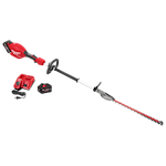 The image shows an M18 FUEL™ Short Pole Hedge Trimmer Kit, which includes a red and black pole hedge trimmer with a long shaft and blade, a battery pack, a charger, and a power cord. The trimmer features a handle for easy grip. All components are arranged neatly for display.