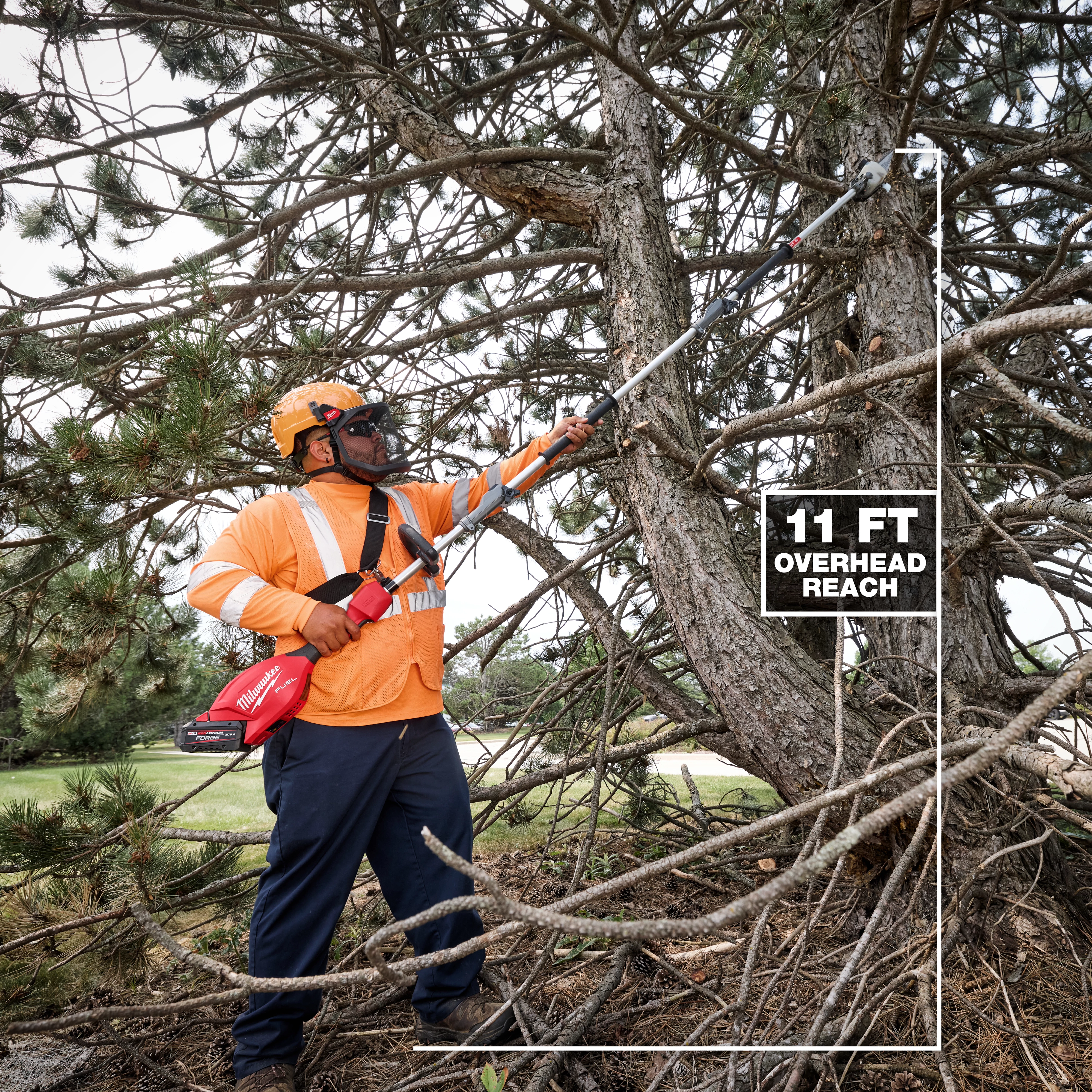 A person in an orange safety outfit and helmet uses the M18 FUEL™ Pole Saw w/ QUIK-LOK™ Kit to trim branches from a large tree. The image highlights the 11-foot overhead reach of the pole saw.