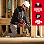 A woman wearing Women's GRIDIRON™ Double Knee Jogger Pants is kneeling on a wooden floor in a construction setting, holding a red power tool. The pants are highlighted for their durable heavyweight fabric and nylon reinforced pocket clip zone. Safety gear includes a white helmet and work boots.